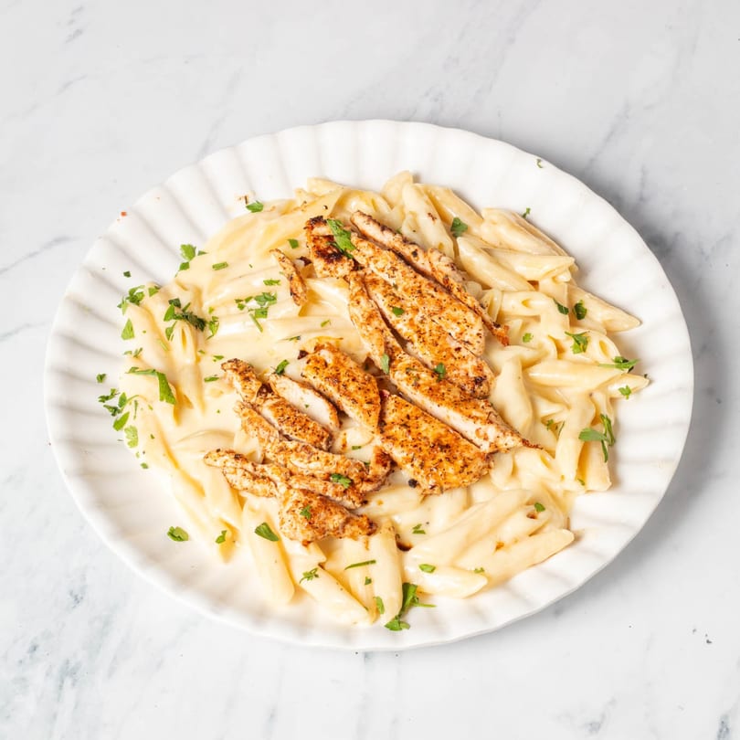 Creamy penne pasta with grilled chicken and parsley on a white plate from St. Lucie West Pizzeria.
