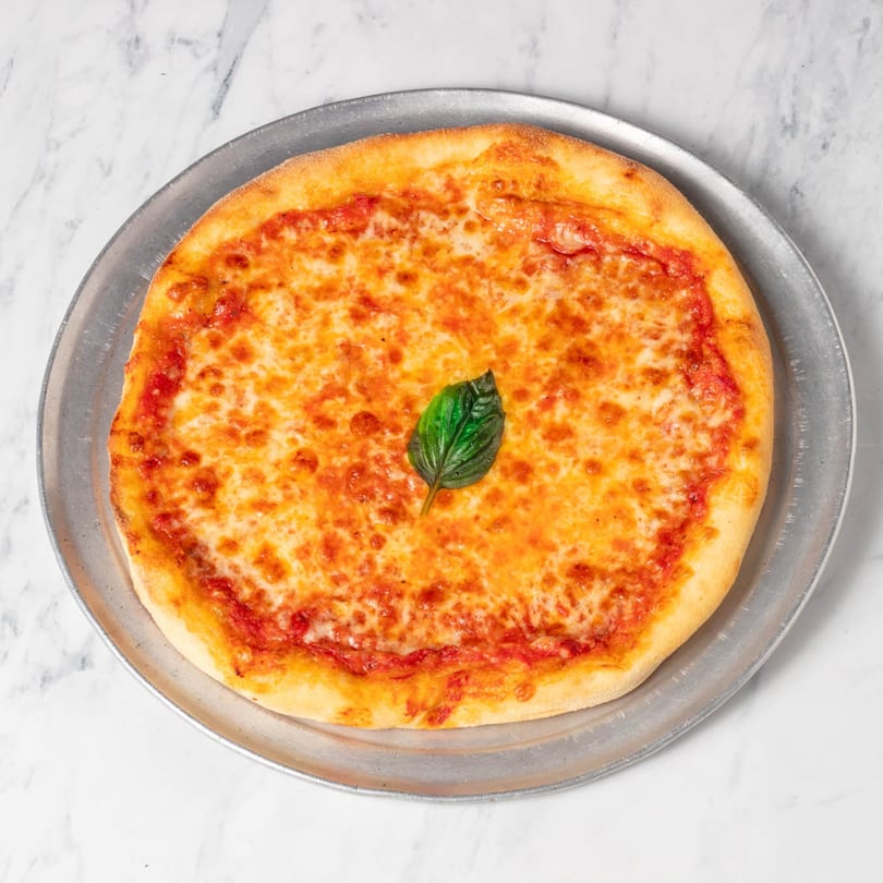 A whole cheese pizza with a single basil leaf on top, on a metal pan.