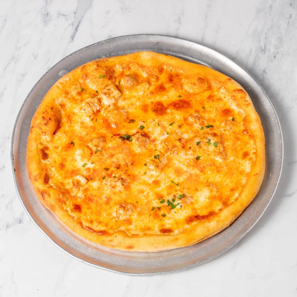 St. Lucie West Pizzeria's buffalo chicken pizza, topped with cheese and parsley, on a metal pan.