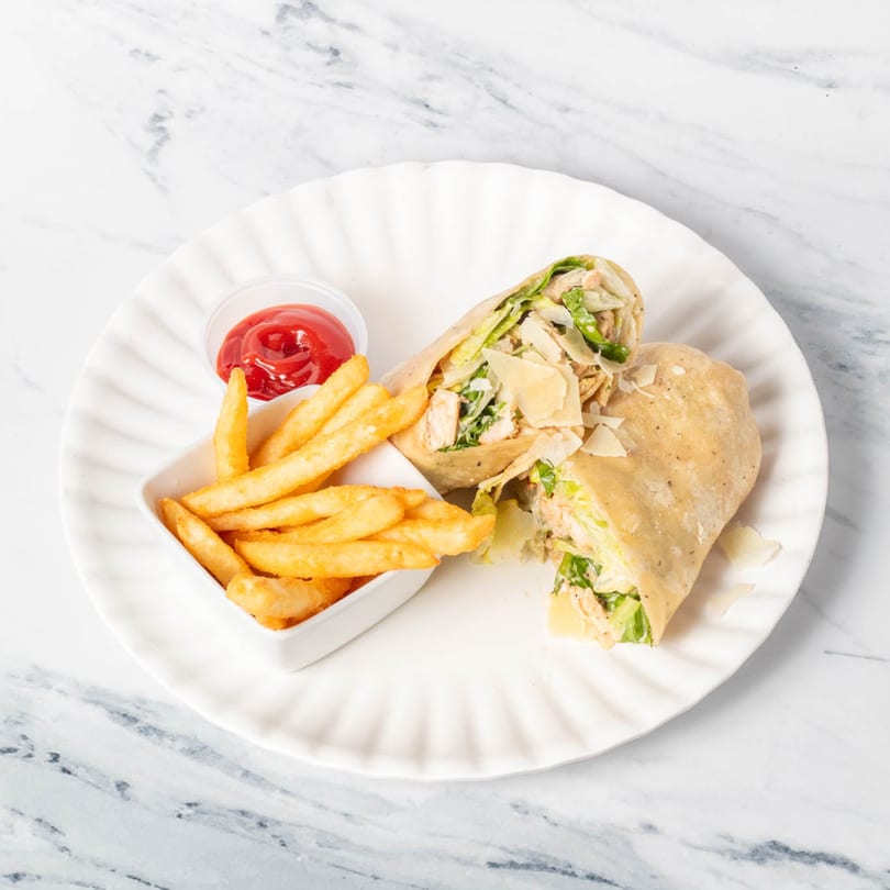 Chicken Caesar wrap, cut in half, with a side of golden fries and ketchup on a white plate.