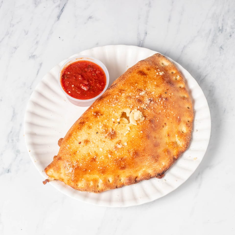 Golden-brown calzone with parmesan cheese and a side of marinara sauce on a white plate.