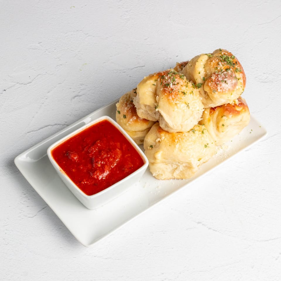 Garlic knots topped with herbs and parmesan cheese, served with a side of marinara sauce.