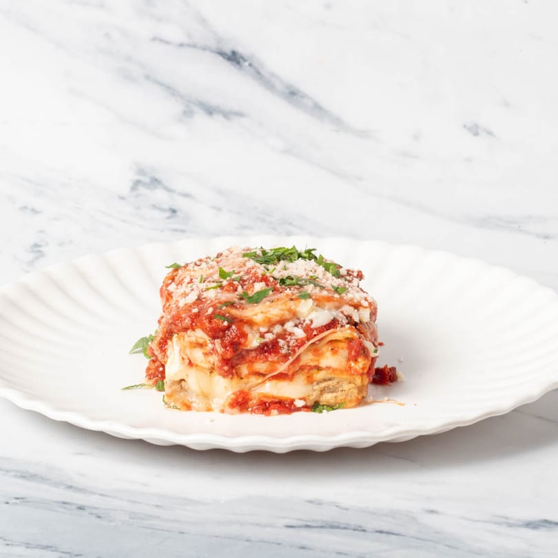 A square serving of St. Lucie West Pizzeria's lasagna, topped with red sauce, cheese, and parsley.